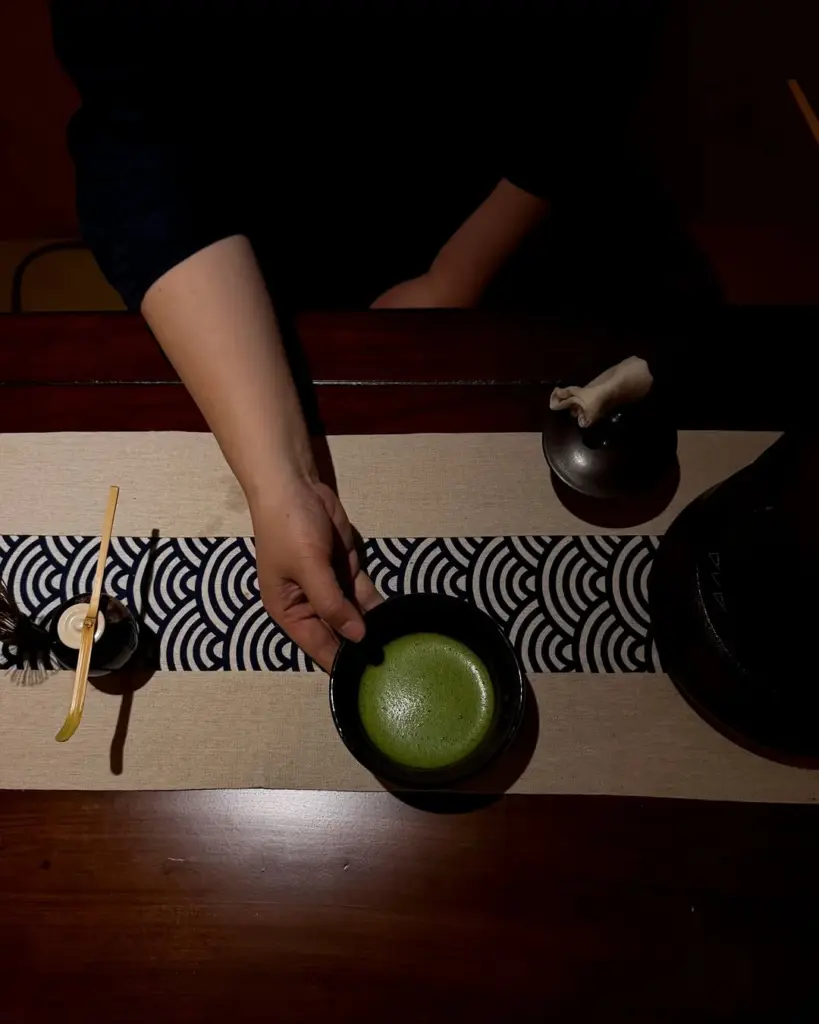Hand placing a dark bowl of foamy green matcha on a table