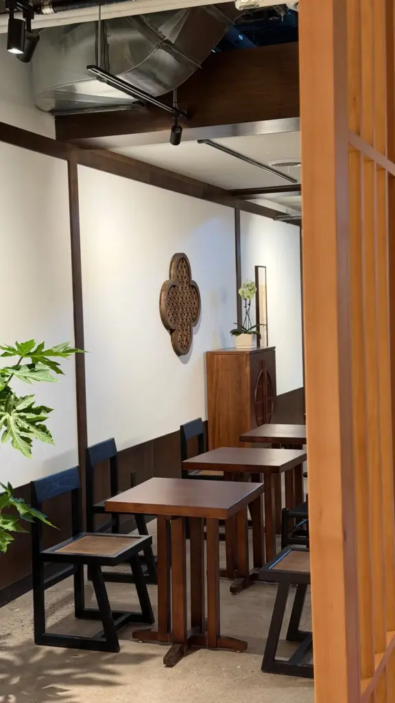 Wooden tables and black chairs beside a slatted partition and potted plants