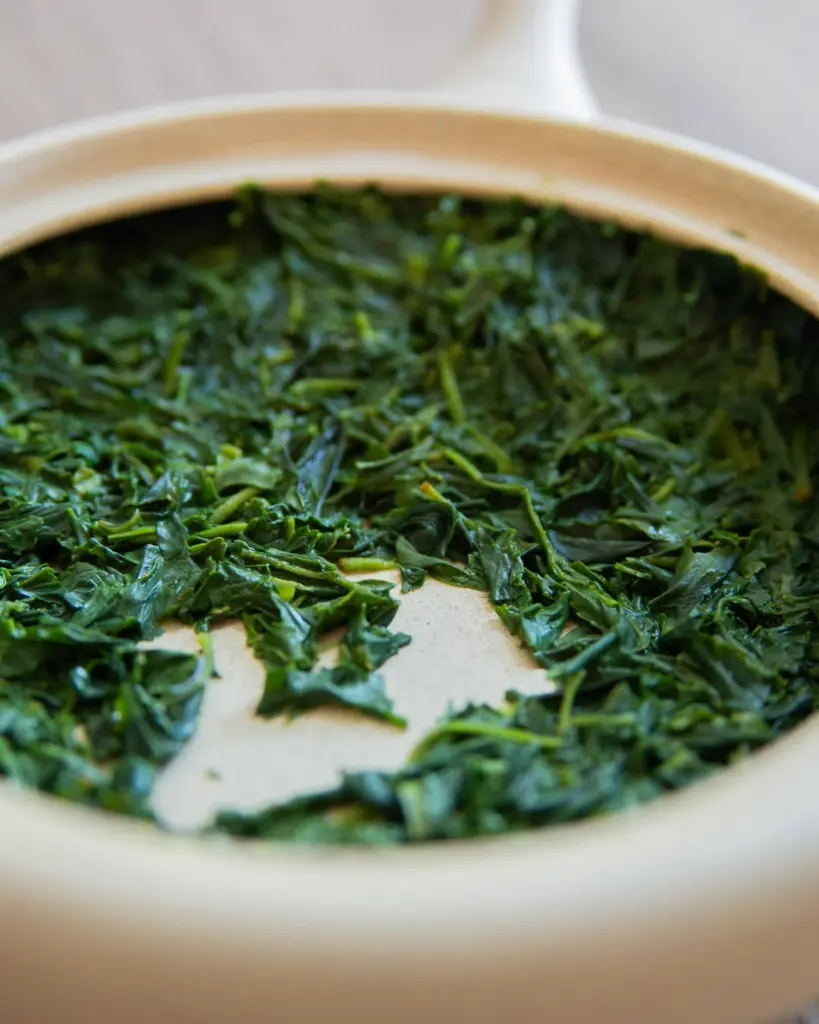 Glossy green steeped tea leaves spread inside a beige ceramic teapot