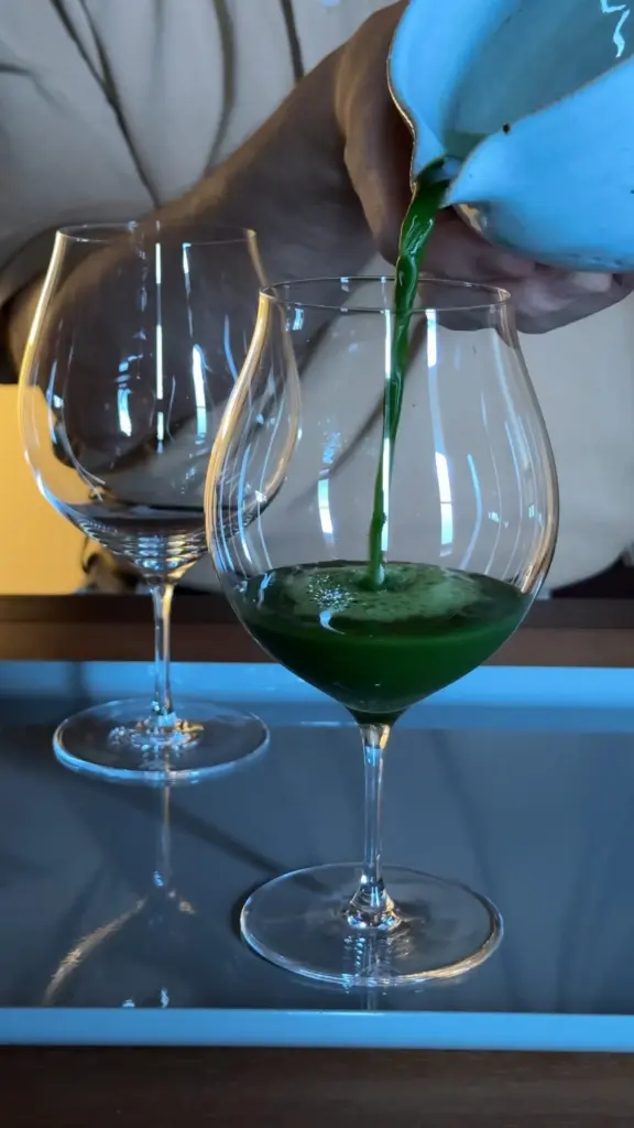 Deep green matcha poured from a blue pitcher into a stemmed glass