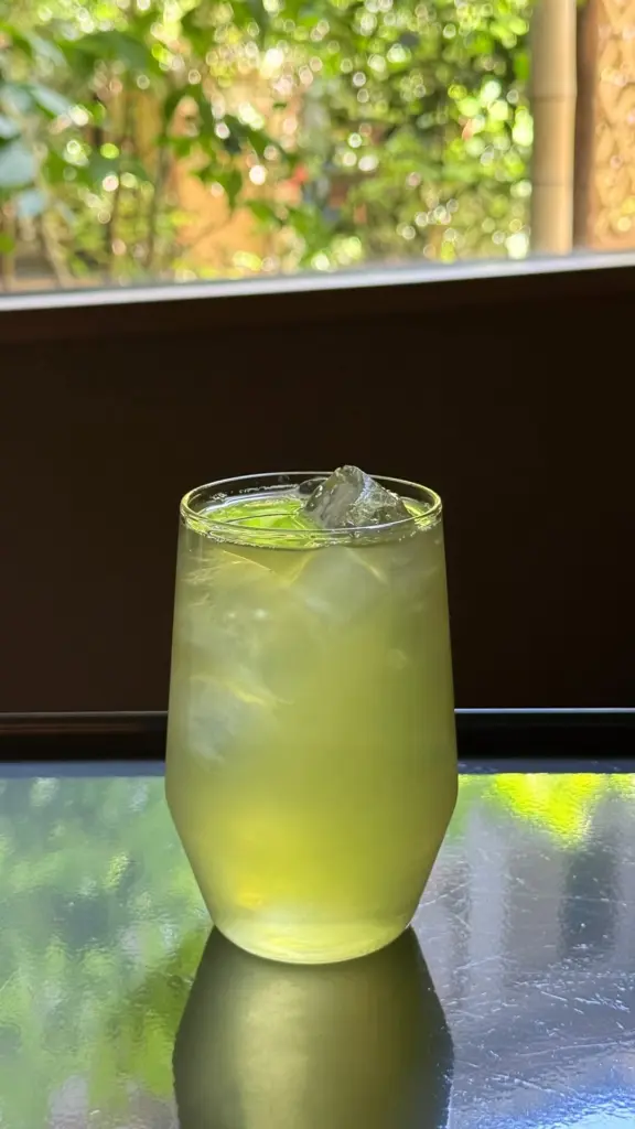 Pale green iced tea in a clear glass by a sunlit window