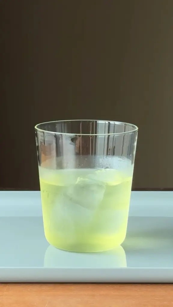 Pale green iced drink in a clear tumbler on a tray