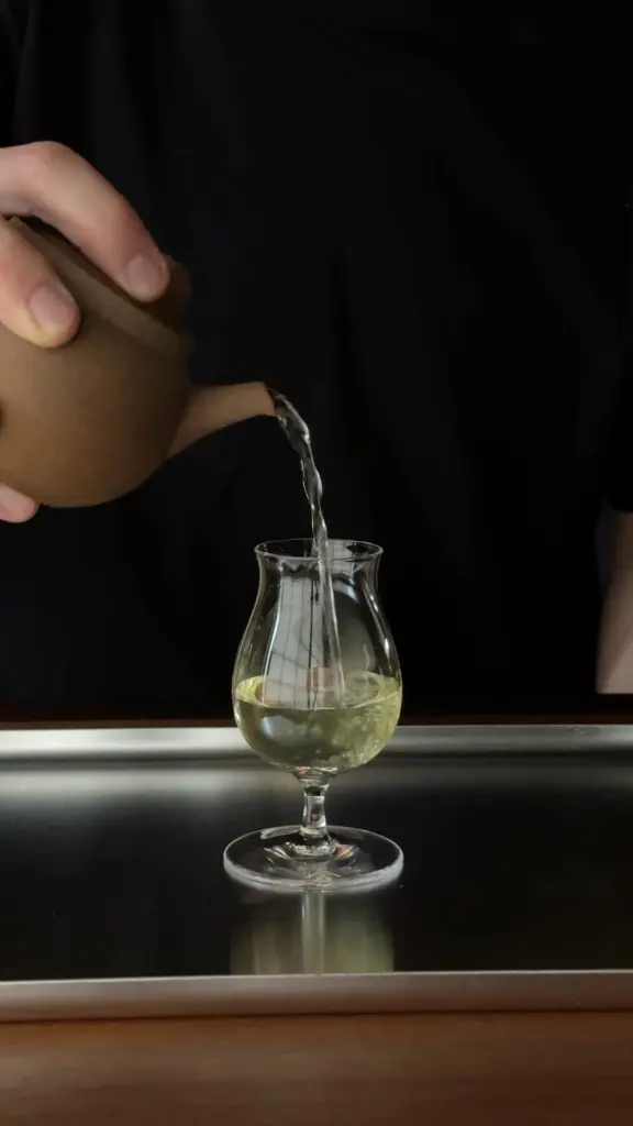 Pale tea poured from a brown teapot into a stemmed glass