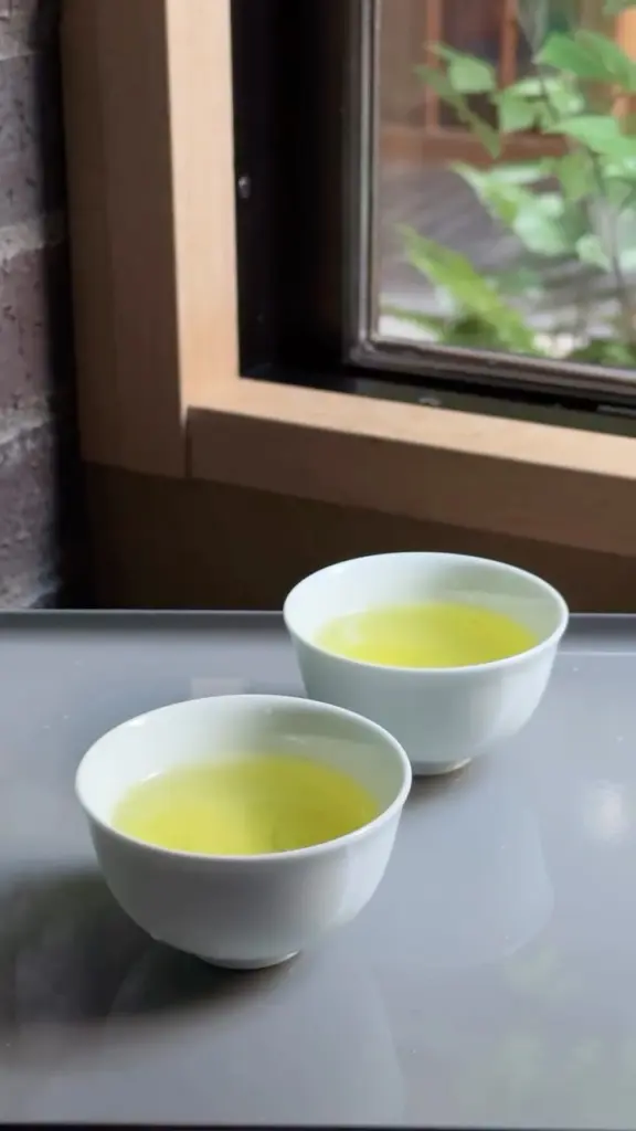 Two white cups filled with pale green tea beside a window