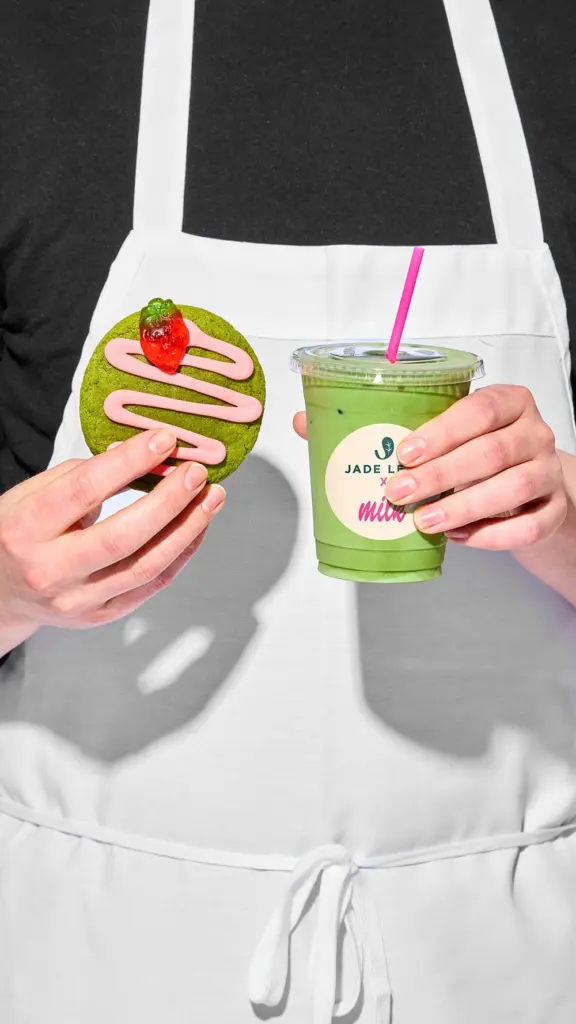 Hands holding an iced green drink and a green cookie with pink icing
