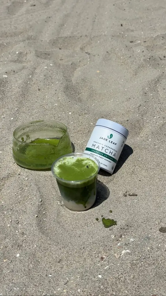 Two green matcha drinks and a Jade Leaf Matcha tin resting on sand