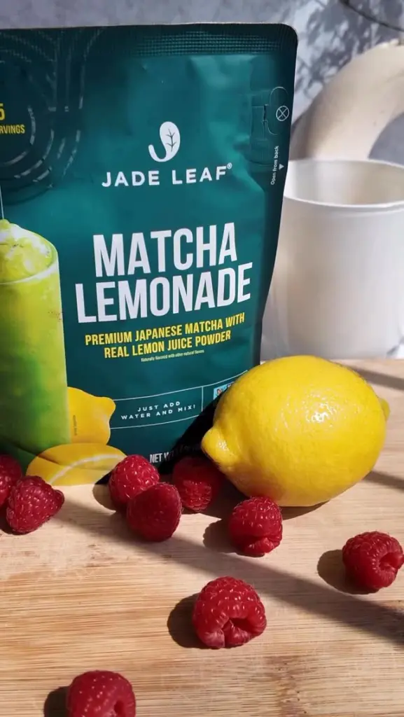 Jade Leaf Matcha Lemonade pouch beside a lemon and scattered raspberries