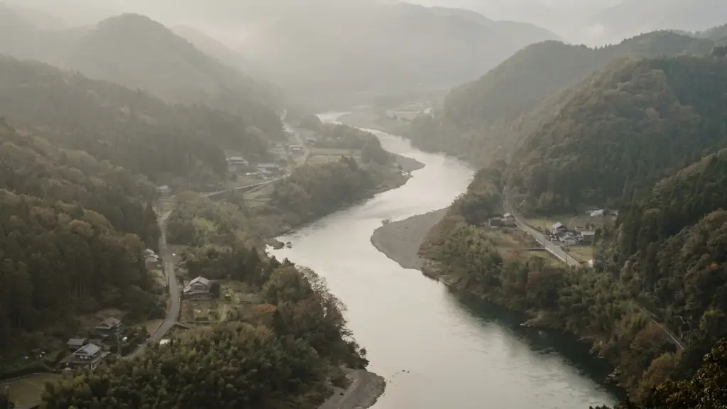 A broad river passes between forested low mountains under soft morning haze.