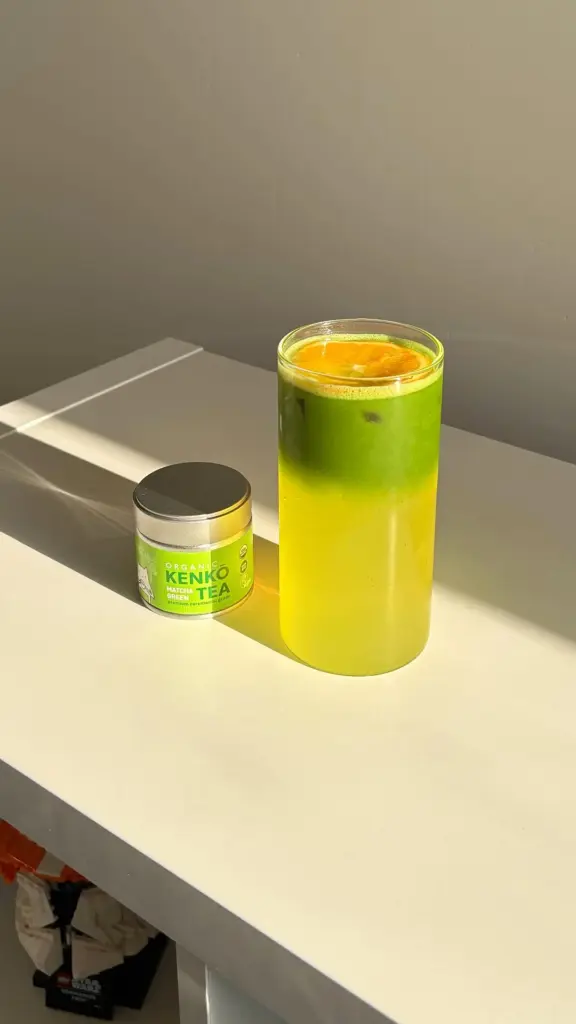 Layered green iced drink with a citrus slice beside a Kenko Tea matcha tin
