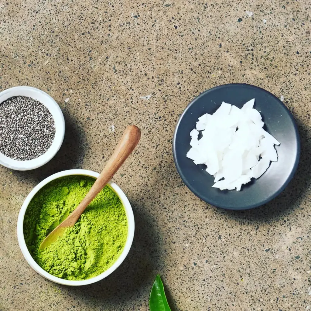 Bowls of green matcha powder, chia seeds, and white coconut flakes