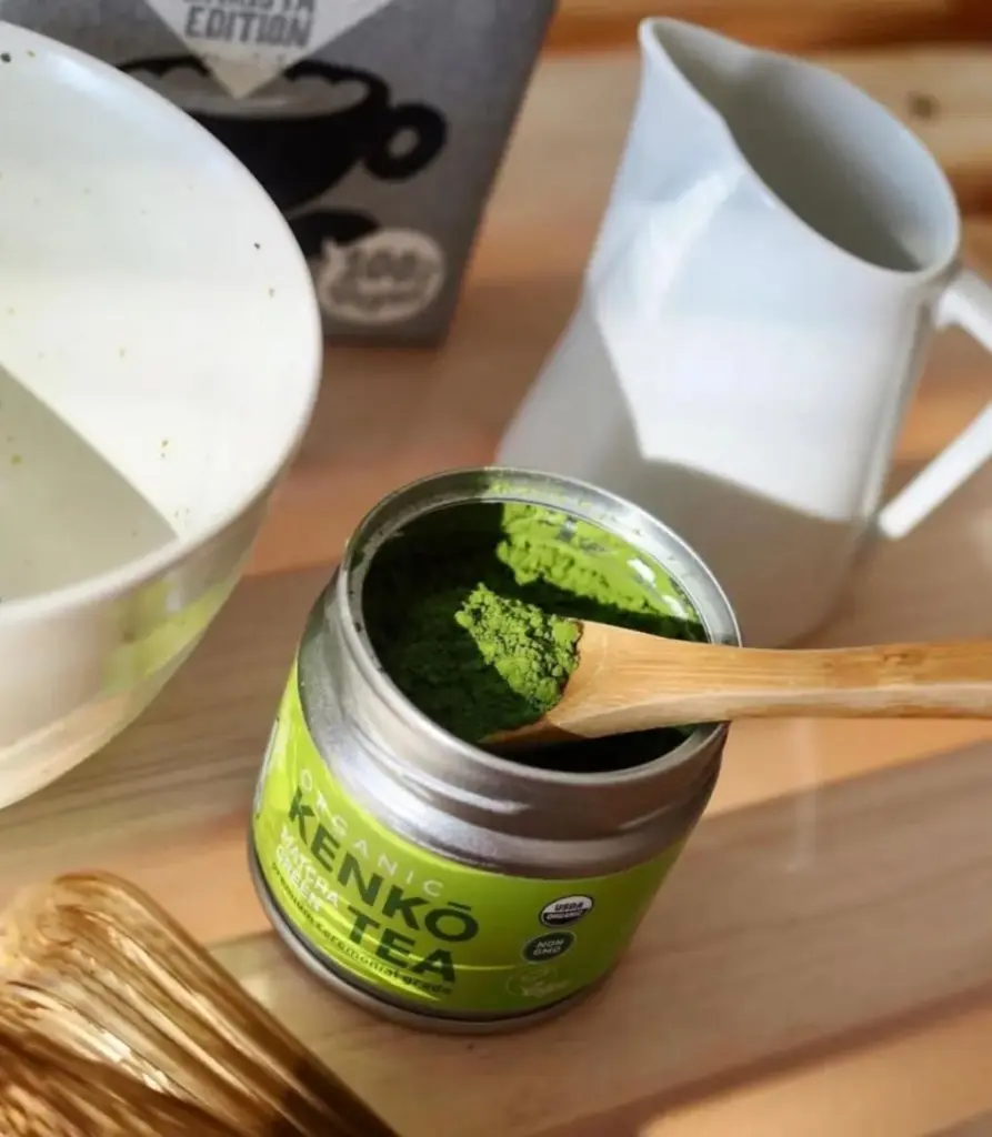 Open Kenko Tea tin filled with bright green matcha and a bamboo scoop