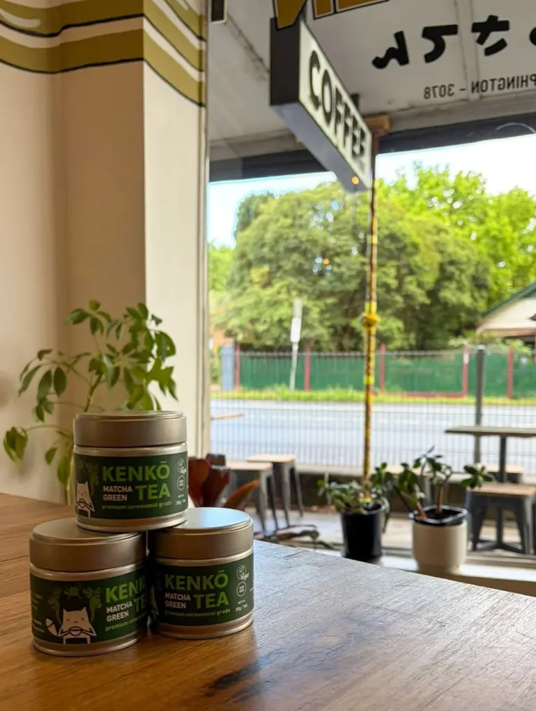 Three stacked Kenko Tea matcha tins on a wooden cafe counter