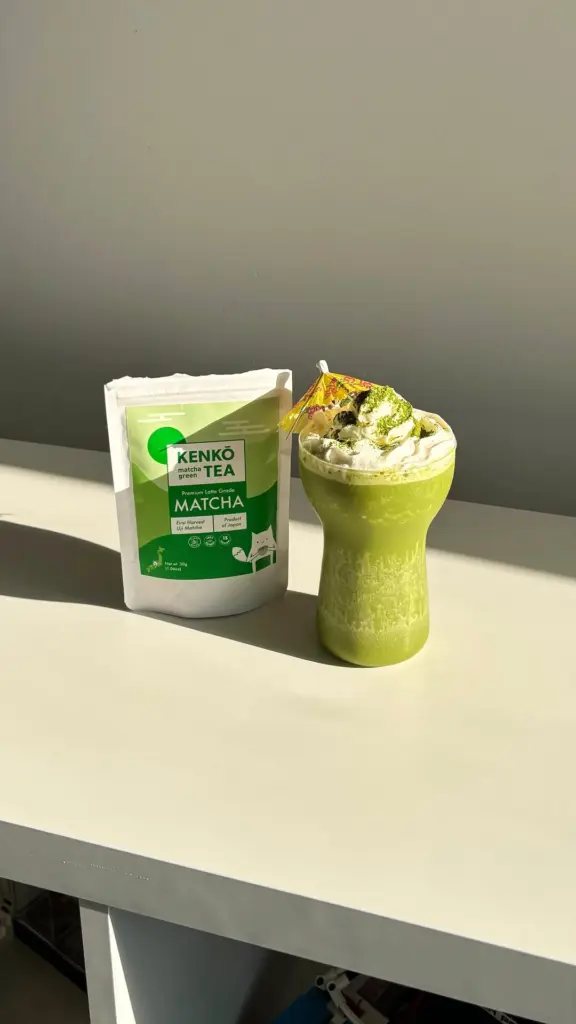 Green iced matcha topped with whipped cream beside a Kenko Tea pouch