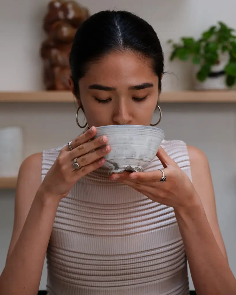 Person holding a gray ceramic tea bowl to their lips