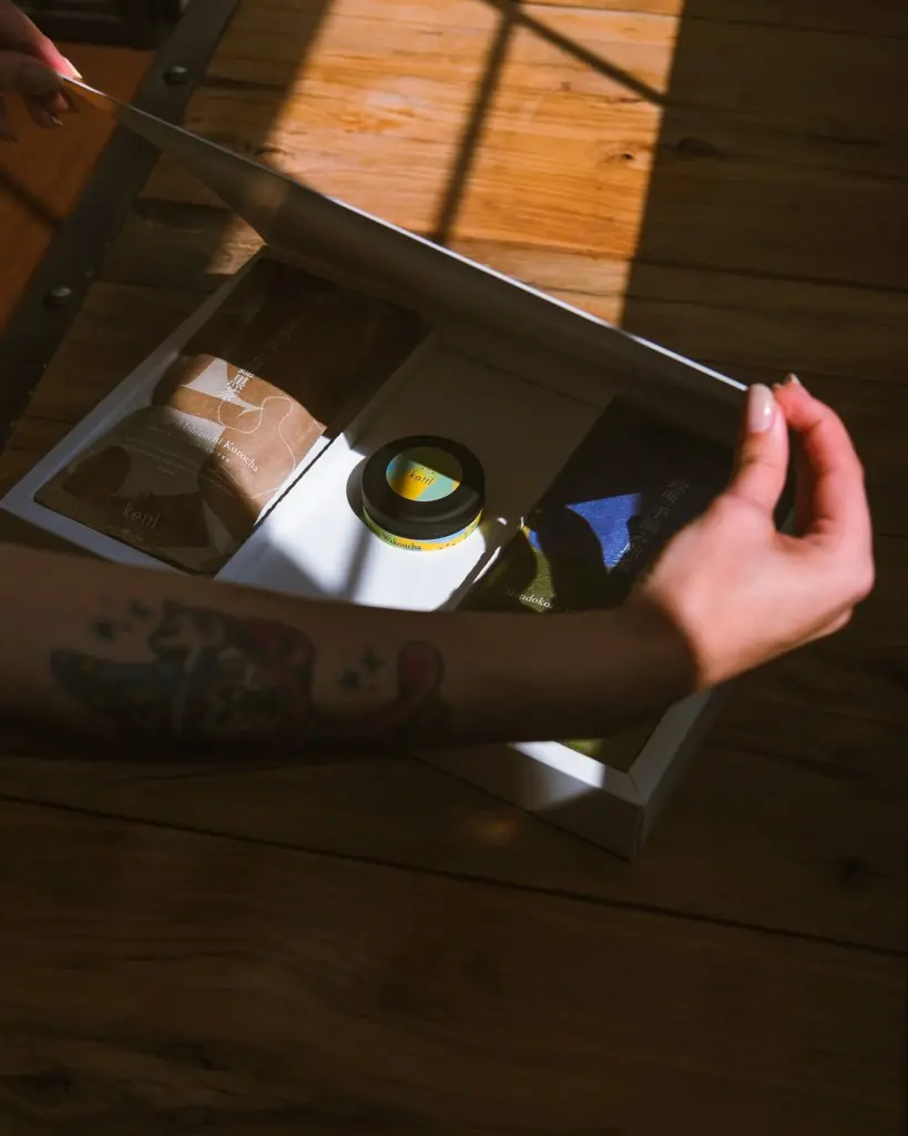 Hands opening a Kettl box containing packaged tea and a small tin
