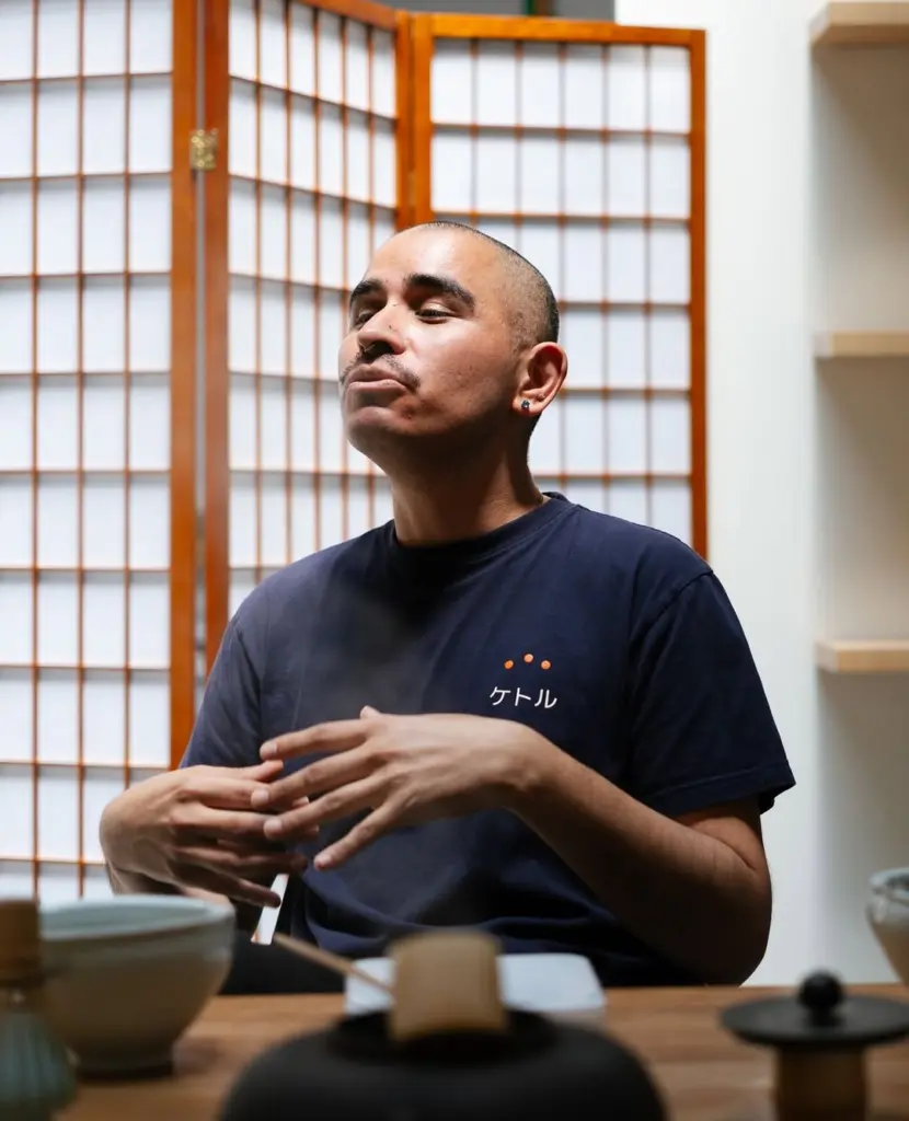 Person in a Kettl T-shirt gesturing behind a table of teaware