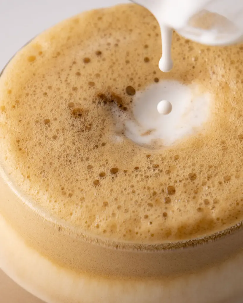 Milk pouring into a glass of frothy brown tea