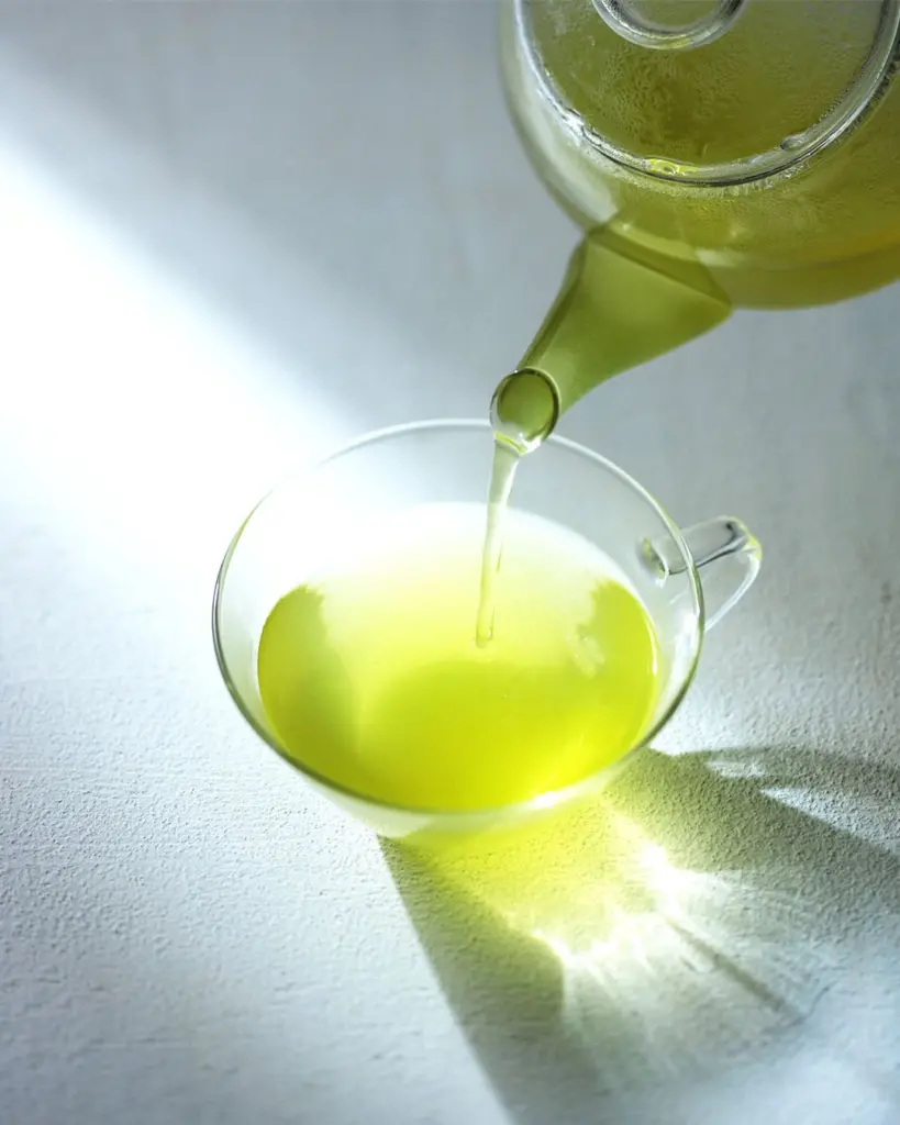 Bright green tea pouring from a glass pot into a clear cup