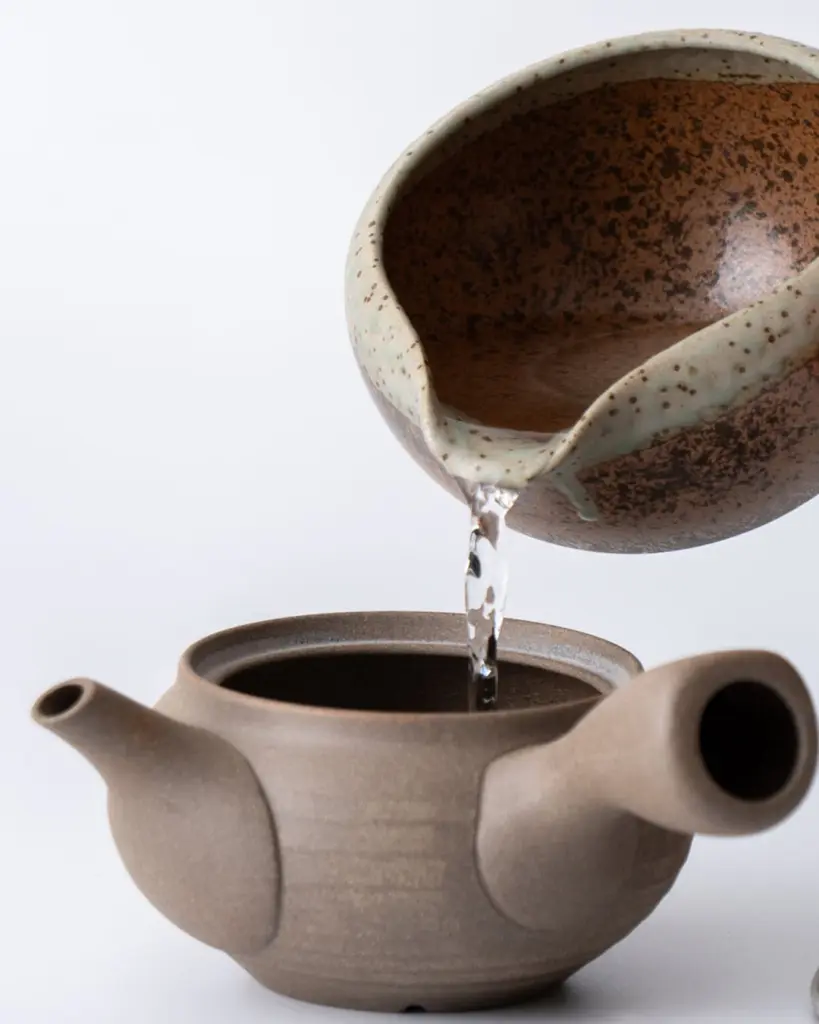 Water pouring from a speckled bowl into a brown clay teapot