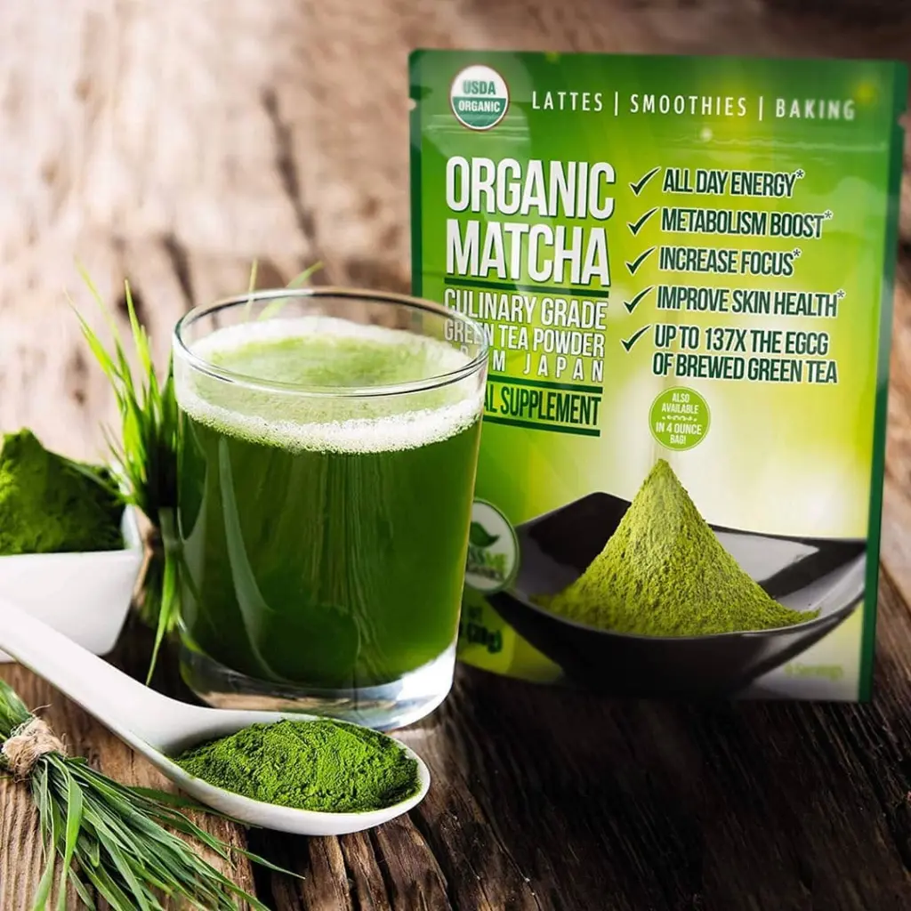 Glass of frothy green drink beside matcha powder and a green matcha pouch
