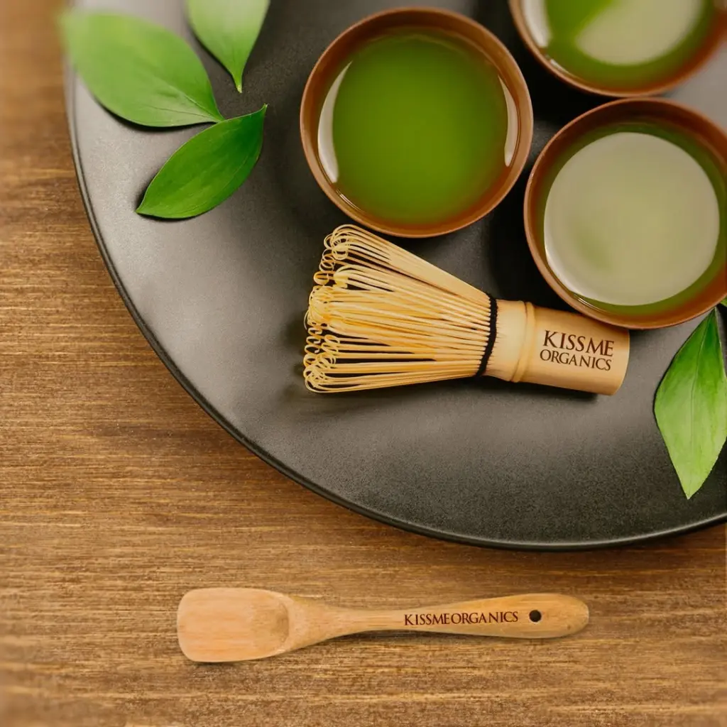 Three bowls of green tea with a bamboo whisk, scoop, and leaves