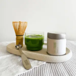 Bamboo whisk, metal scoop, green matcha drink, and Tsuki Vanille tin arranged on a tray