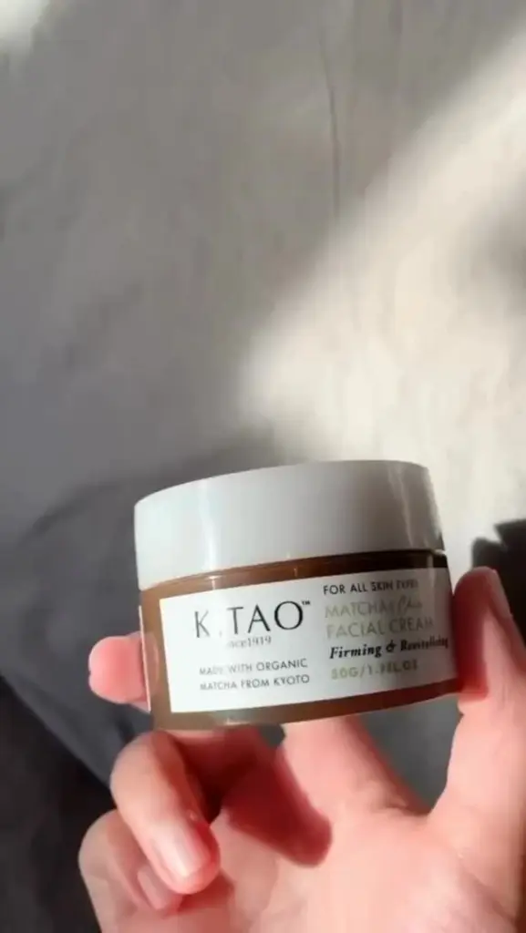 Hand holding a brown jar of Kitao Matcha & Chia Facial Cream in sunlight