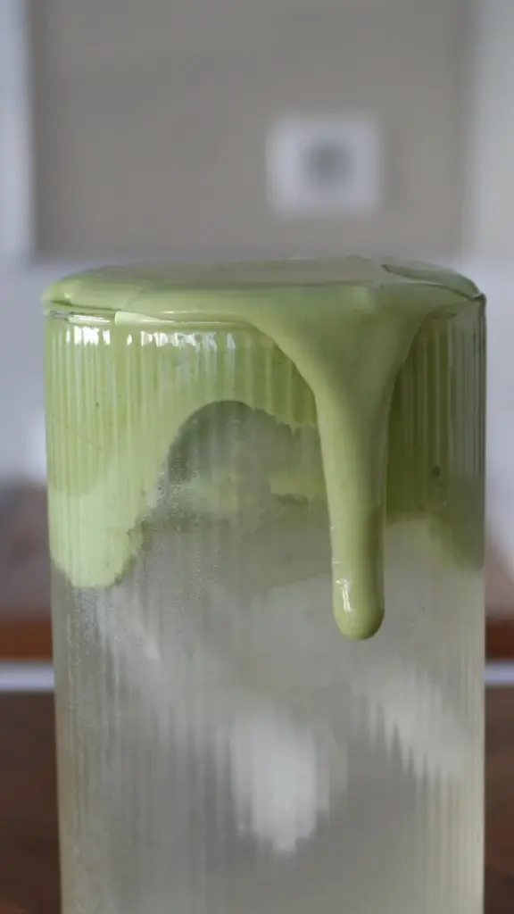 Thick green matcha dripping over a chilled ribbed glass