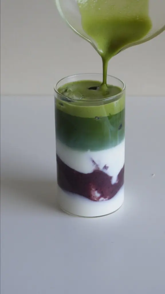 Matcha pouring into an iced drink with white and purple layers