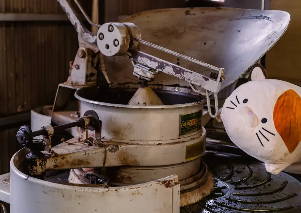 White and orange cat plush beside a weathered round metal processing machine
