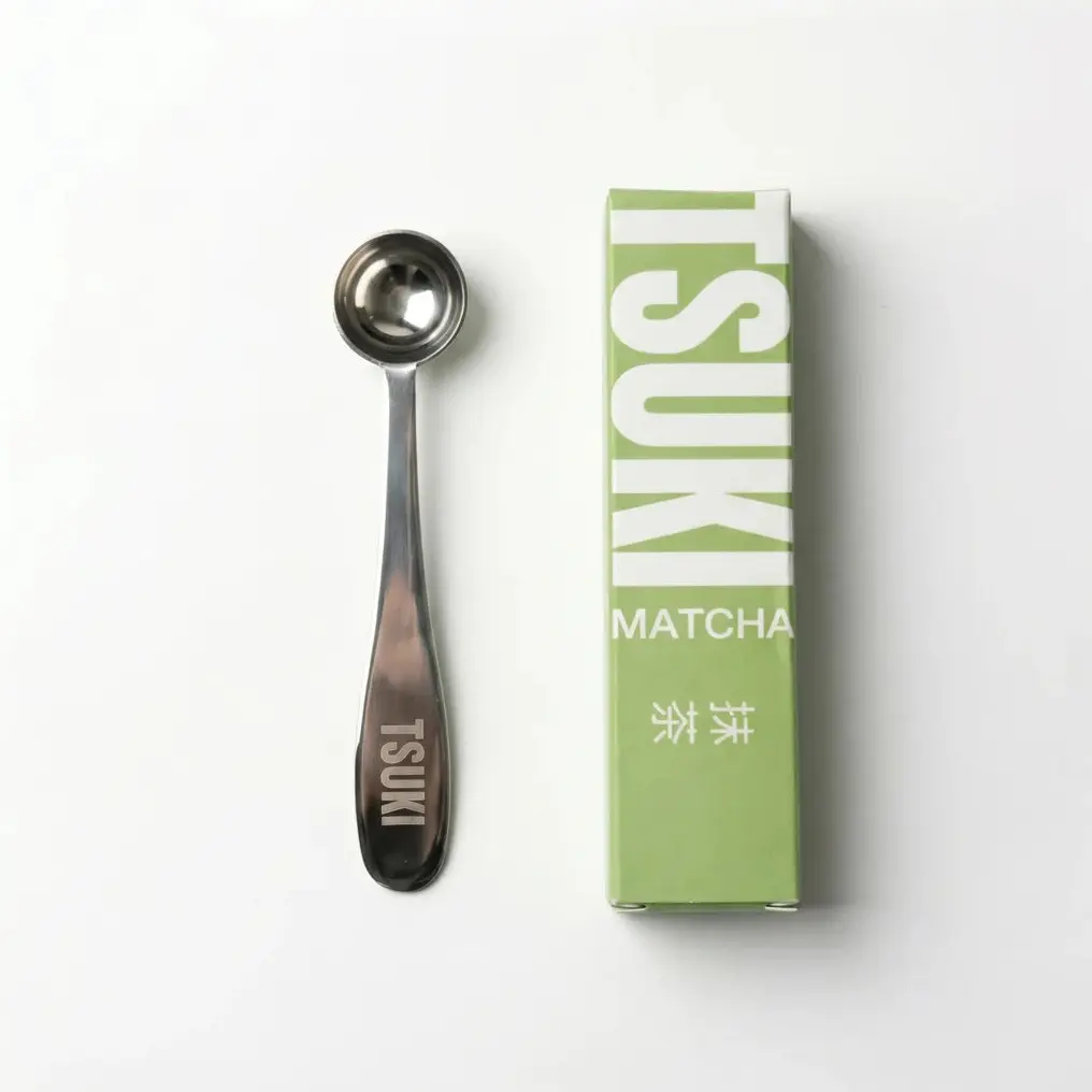 Metal Tsuki measuring spoon beside a green and white Tsuki Matcha box