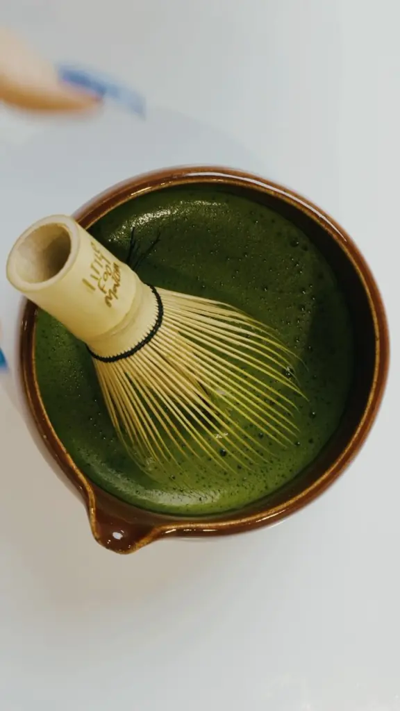 Bamboo whisk resting in a brown bowl of frothy green matcha