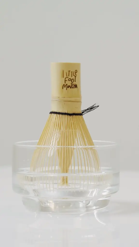 Branded bamboo matcha whisk standing in a clear bowl of water