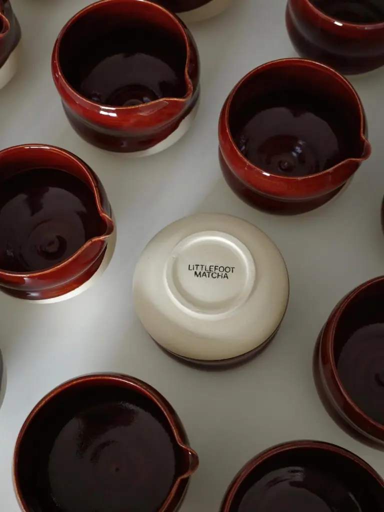Red glazed ceramic pouring bowls surrounding an upside-down branded bowl