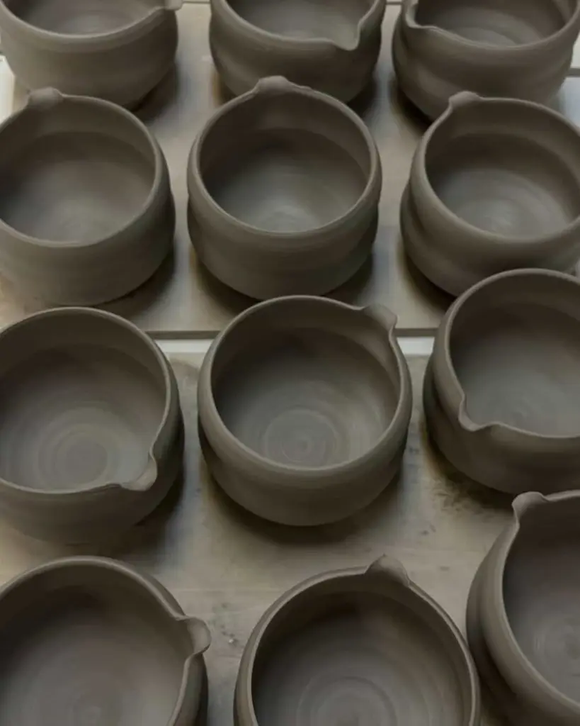 Rows of unglazed gray ceramic bowls with small pouring spouts
