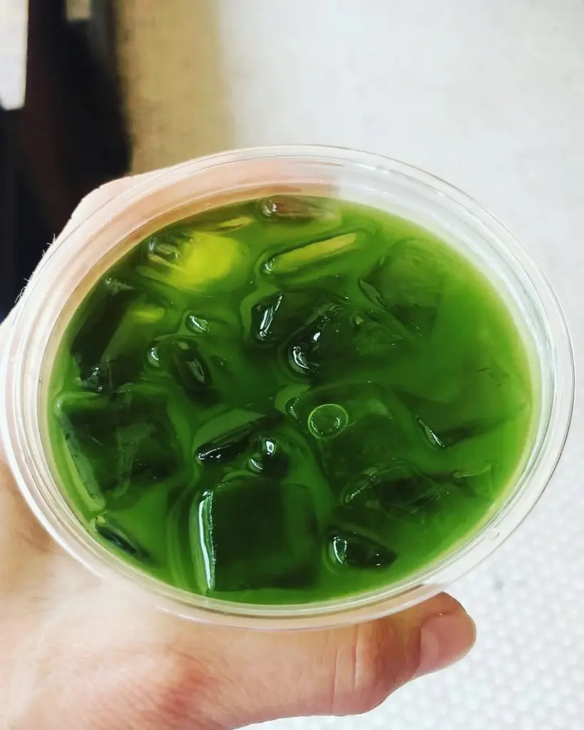Hand holding a clear cup of bright green iced tea