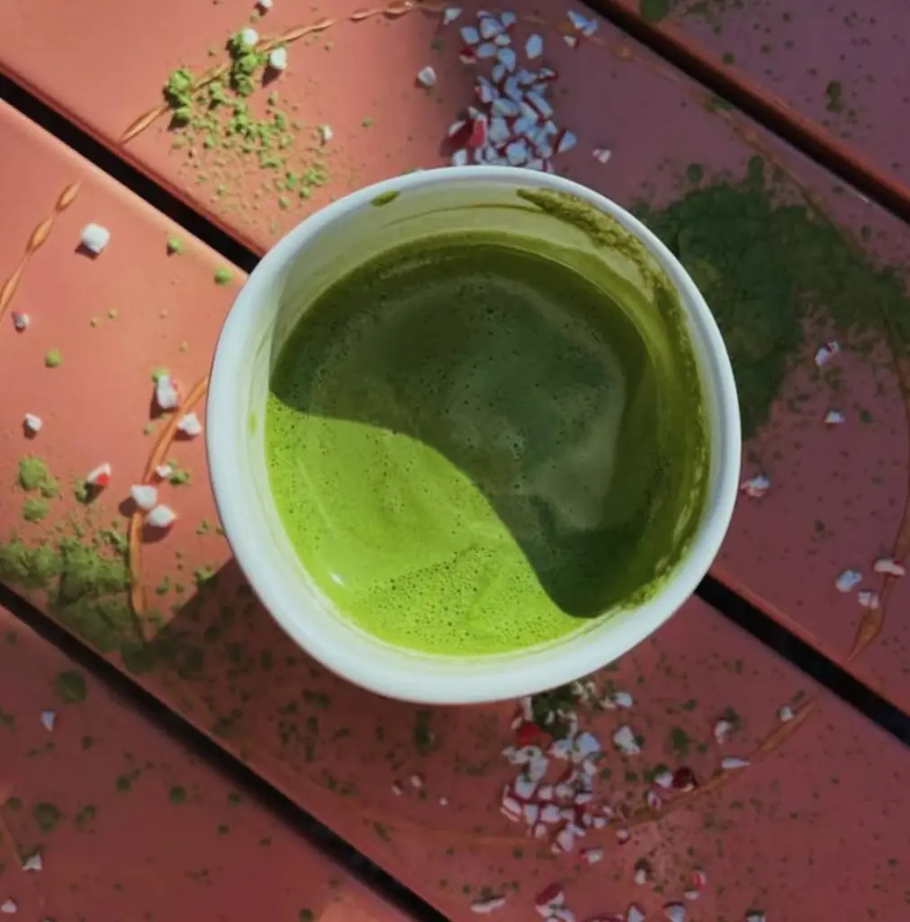 White cup of frothy green matcha on a sunlit red table