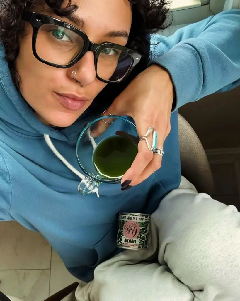 Person in a blue hoodie holding a glass cup of green matcha