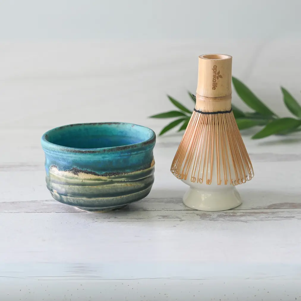 Blue and cream glazed matcha bowl beside a bamboo whisk resting upside down on a white ceramic whisk holder