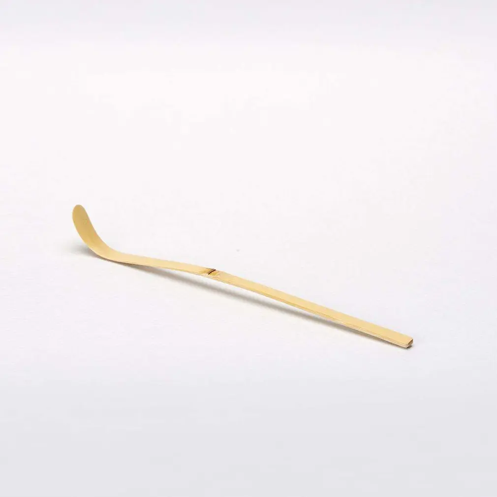 Long pale bamboo matcha scoop with a curved tip on a white background