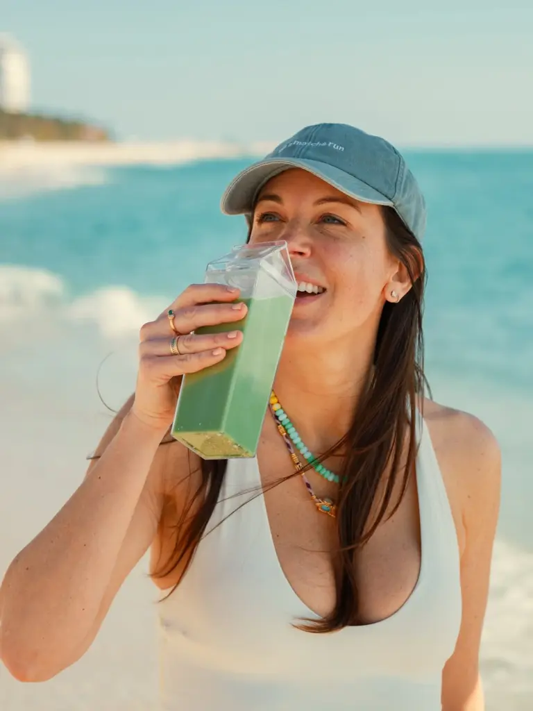 Smiling woman holding a tall green drink by turquoise water