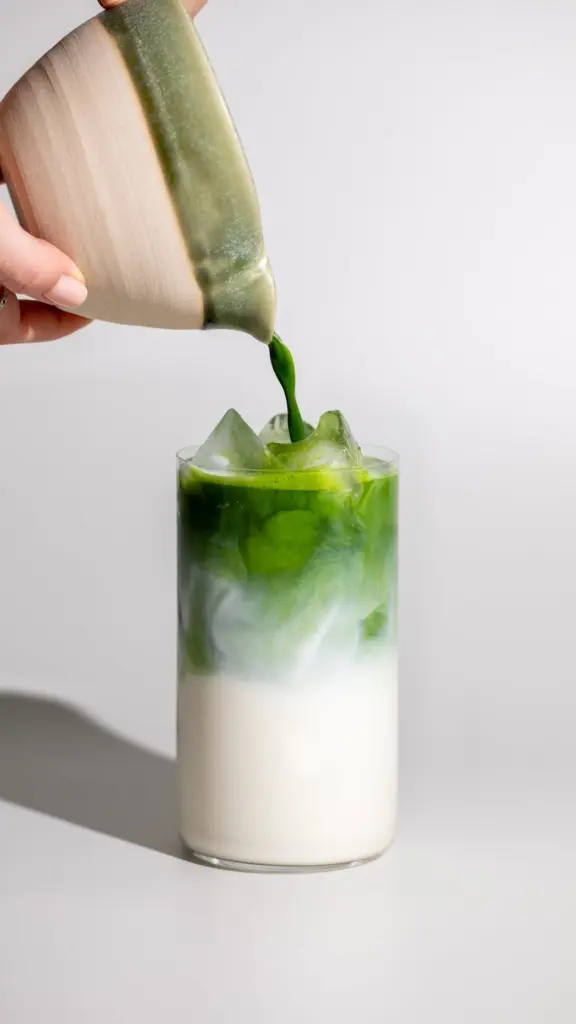 Bright green liquid poured over ice and milk in a tall glass