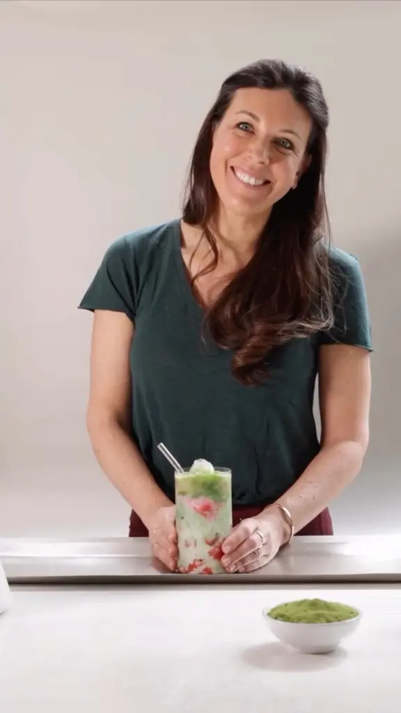 Smiling woman holding a layered iced green drink with red fruit pieces