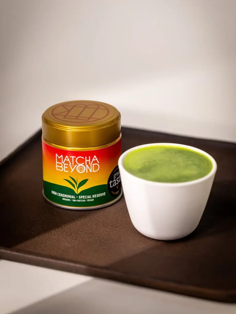 Matcha & Beyond tin beside a white cup filled with a frothy green drink