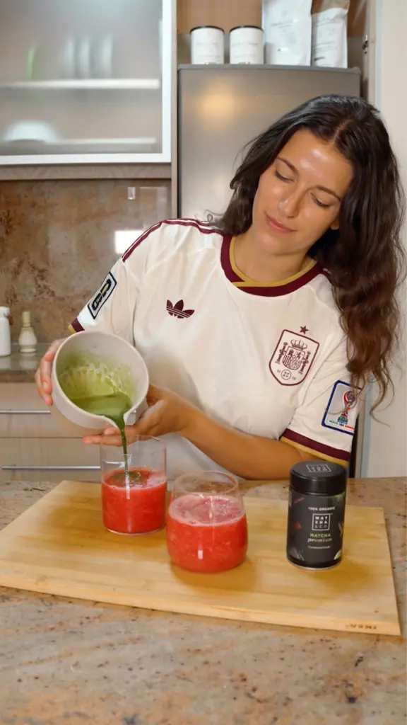 Person pouring green matcha mixture into two glasses of red fruit drink