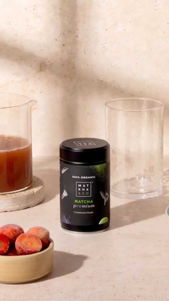 Black Matcha Premium tin beside strawberries, a pitcher, and an empty glass