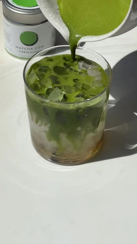 Green matcha being poured over ice in a glass