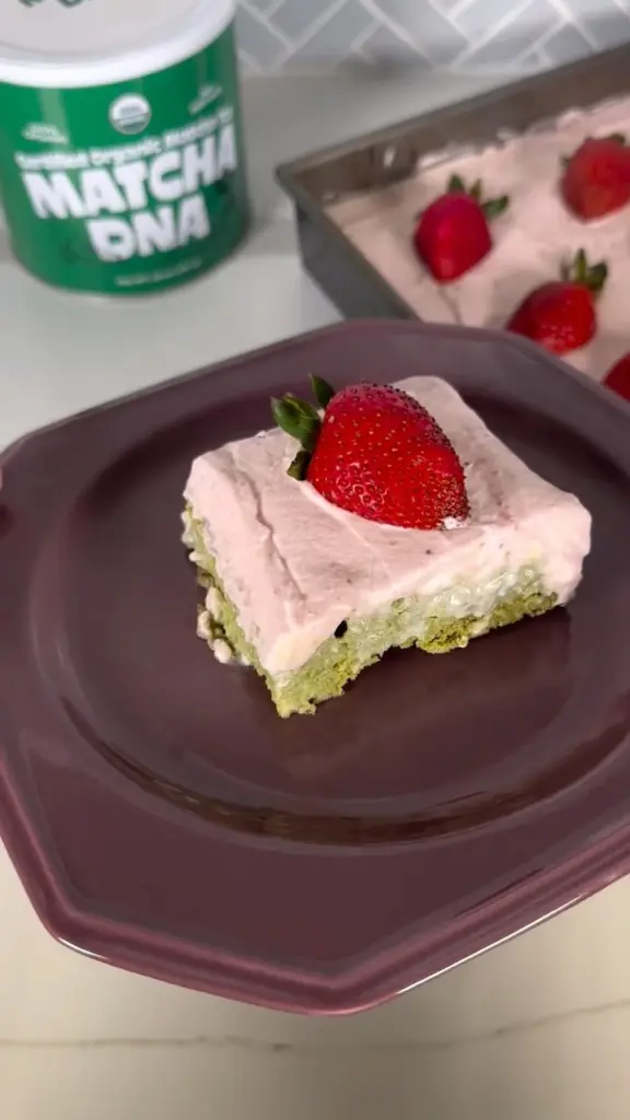Layered green and pink dessert topped with a whole strawberry on a purple plate