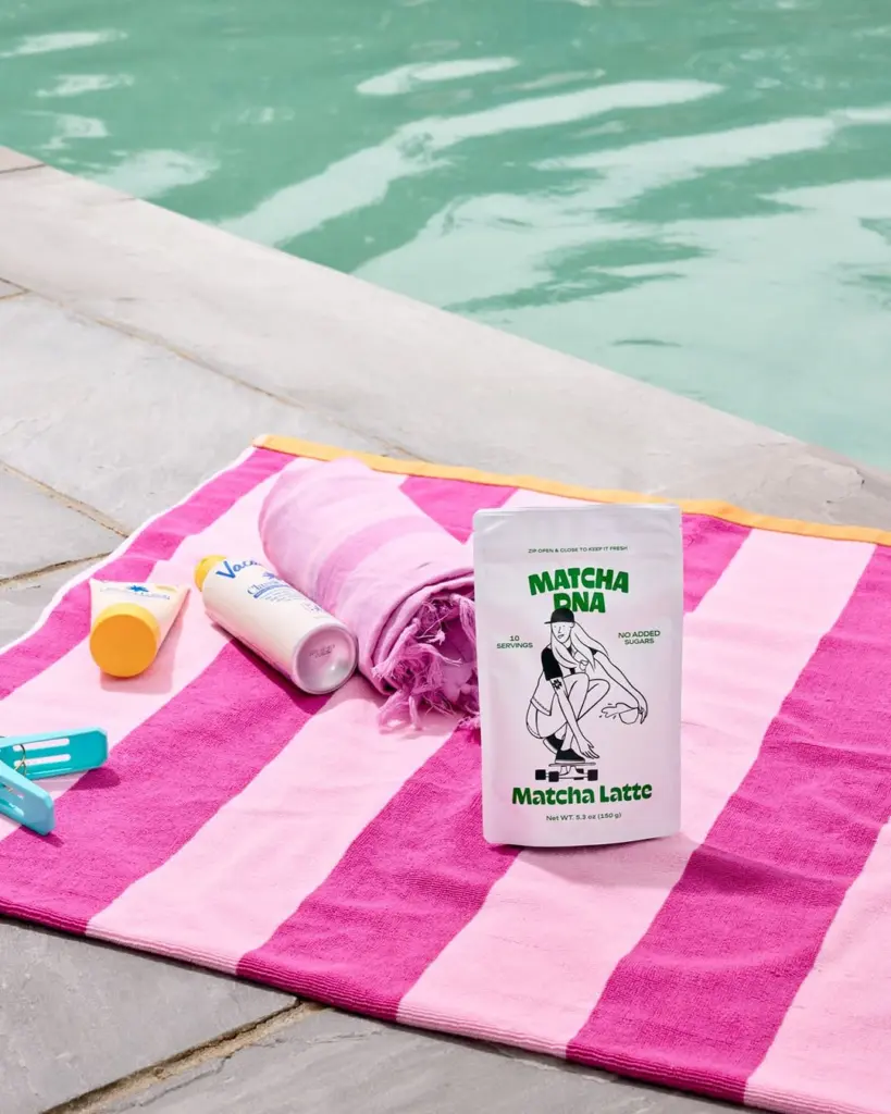Matcha DNA Matcha Latte pouch on a pink striped towel beside a pool