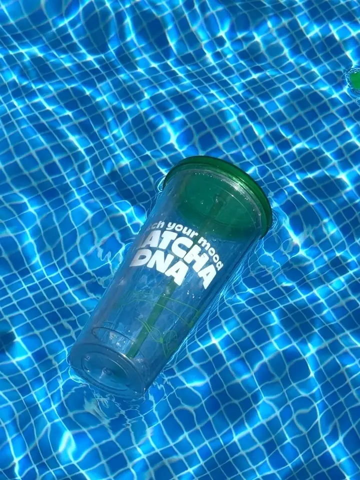 Clear Matcha DNA tumbler with green lid floating in blue, sunlit water